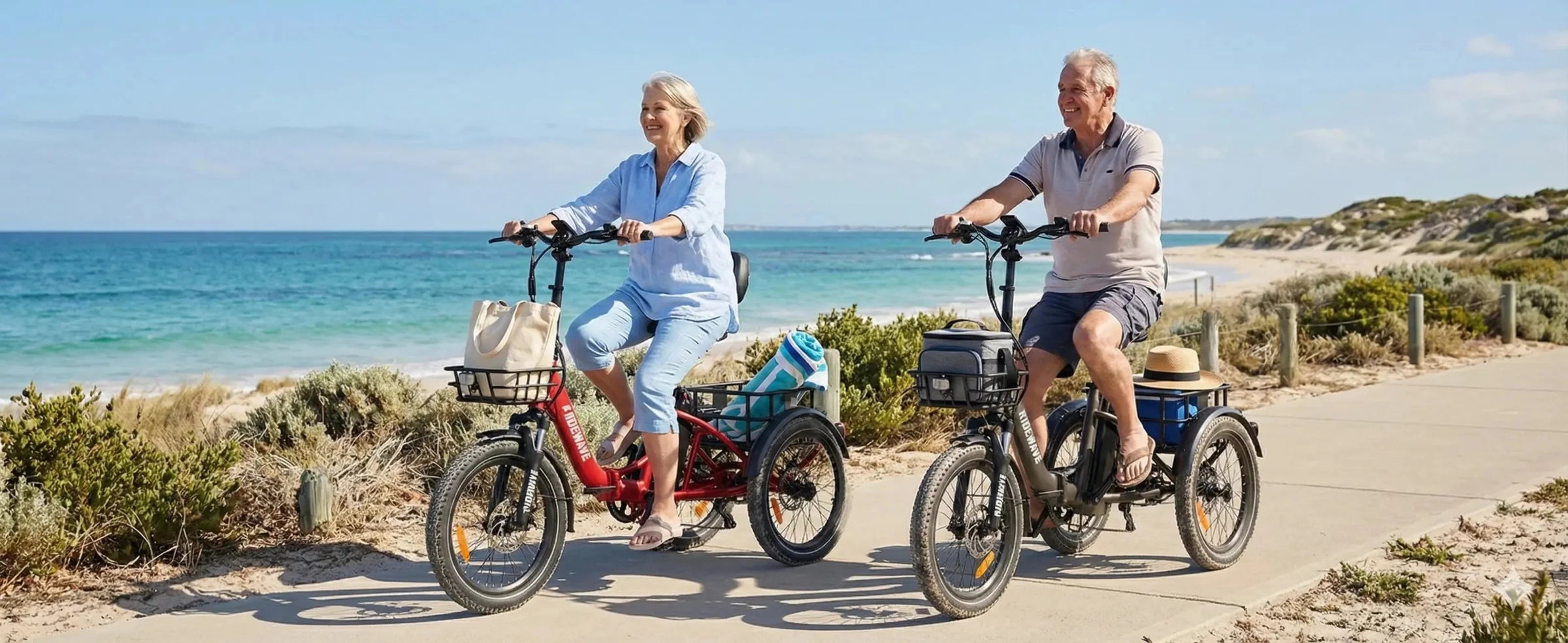 Two adults riding Ridewave electric tricycles on a coastal bike path, enjoying a stable and comfortable ride.