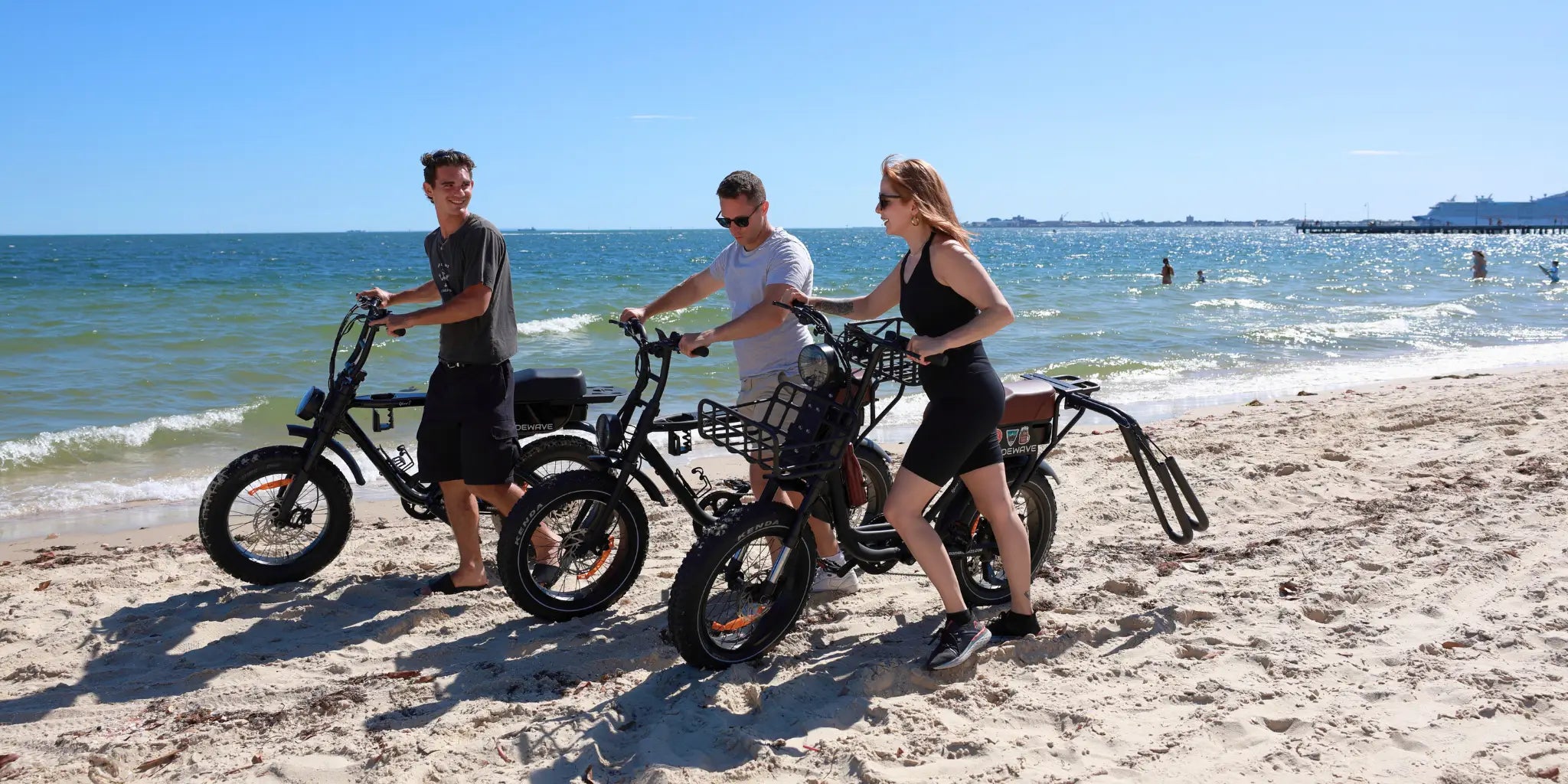 Fat tyre electric bikes parked outdoors with people standing in front, featuring wide tyres for all-terrain riding